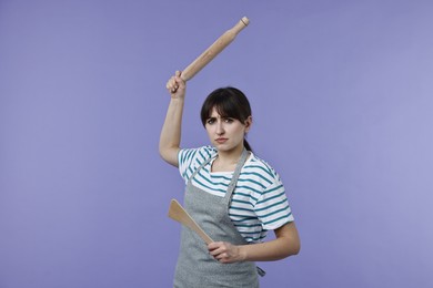 Photo of Woman with rolling pin and turner on violet background