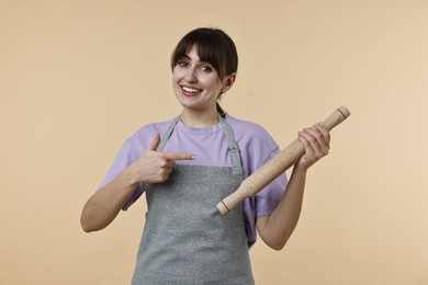 Photo of Woman pointing at rolling pin on beige background