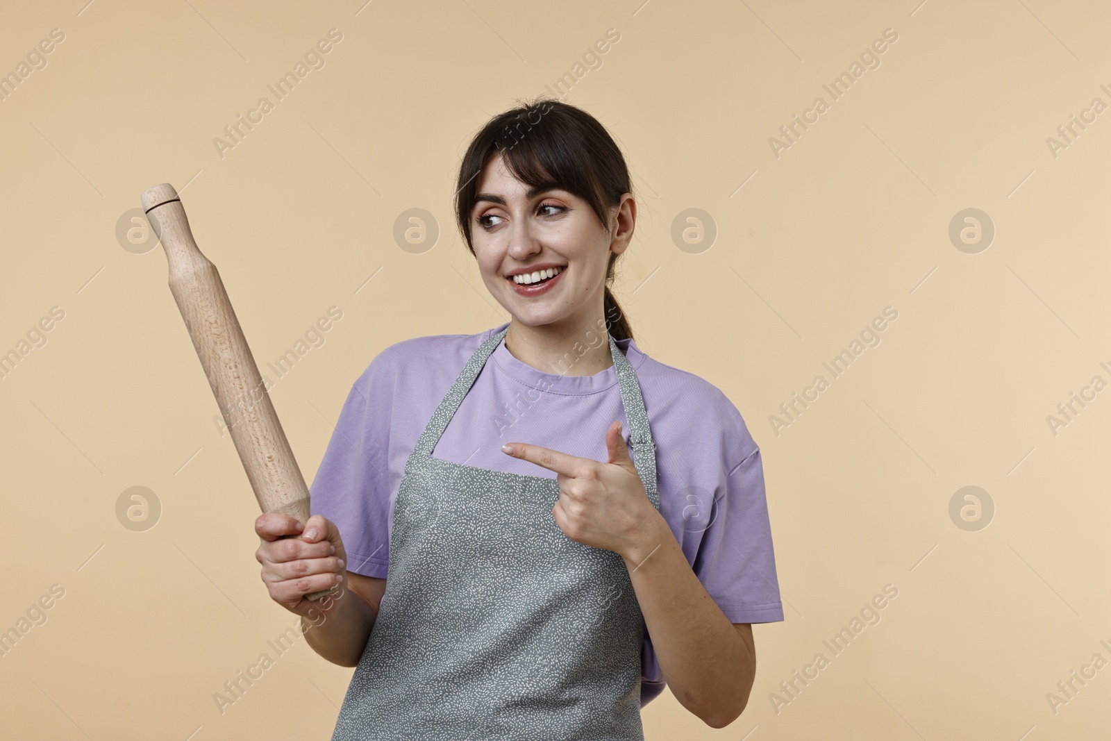 Photo of Woman pointing at rolling pin on beige background