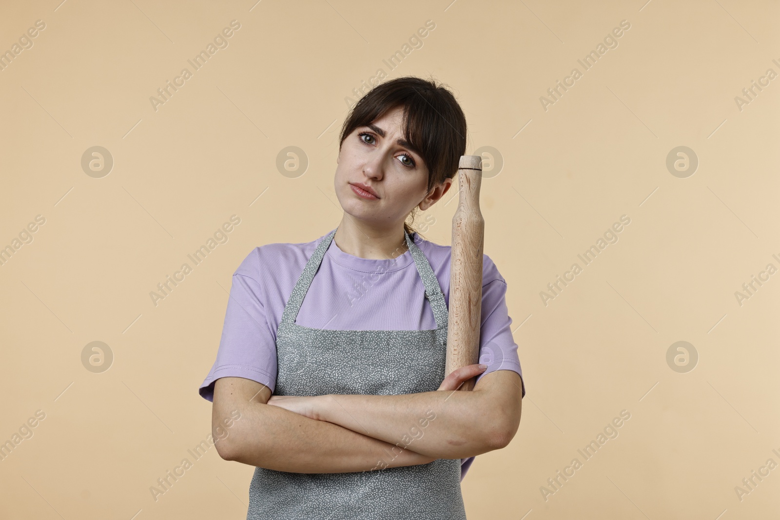 Photo of Upset woman with rolling pin on beige background