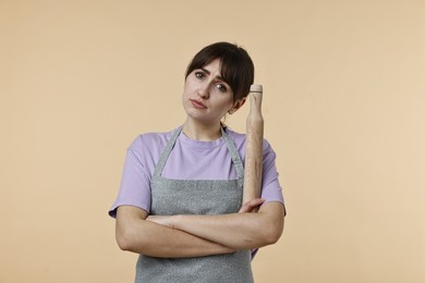 Photo of Upset woman with rolling pin on beige background