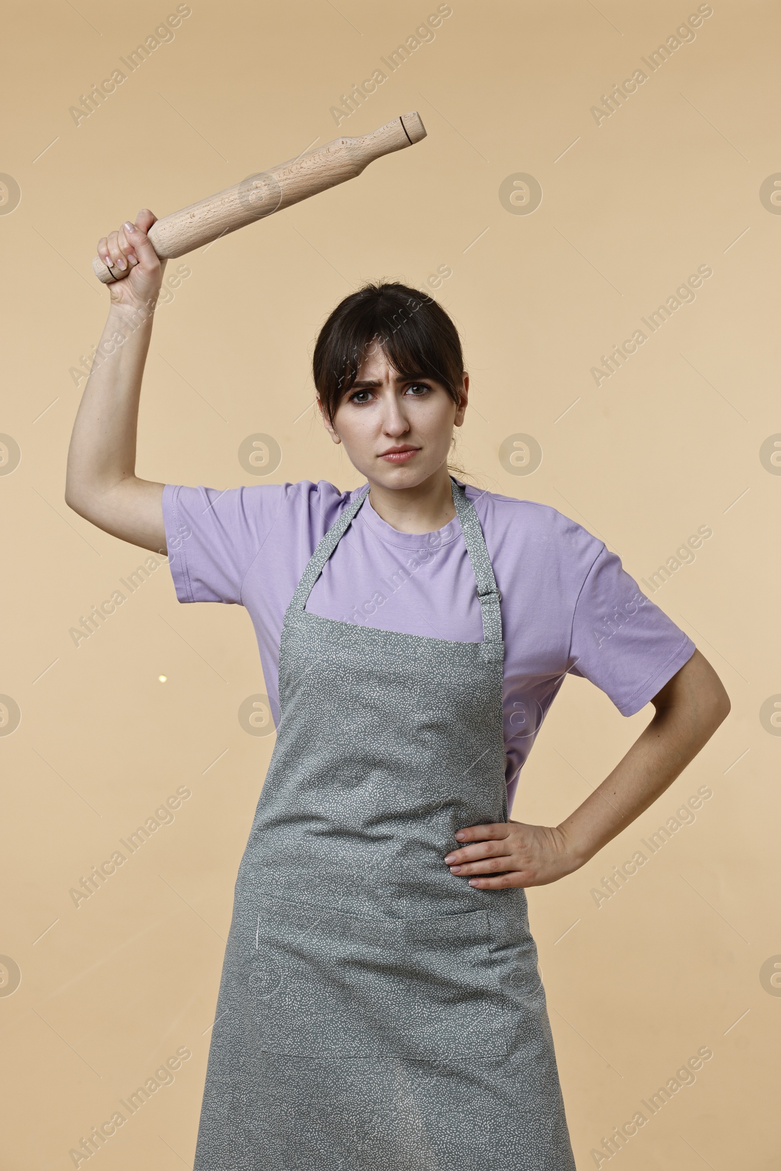 Photo of Angry woman with rolling pin on beige background