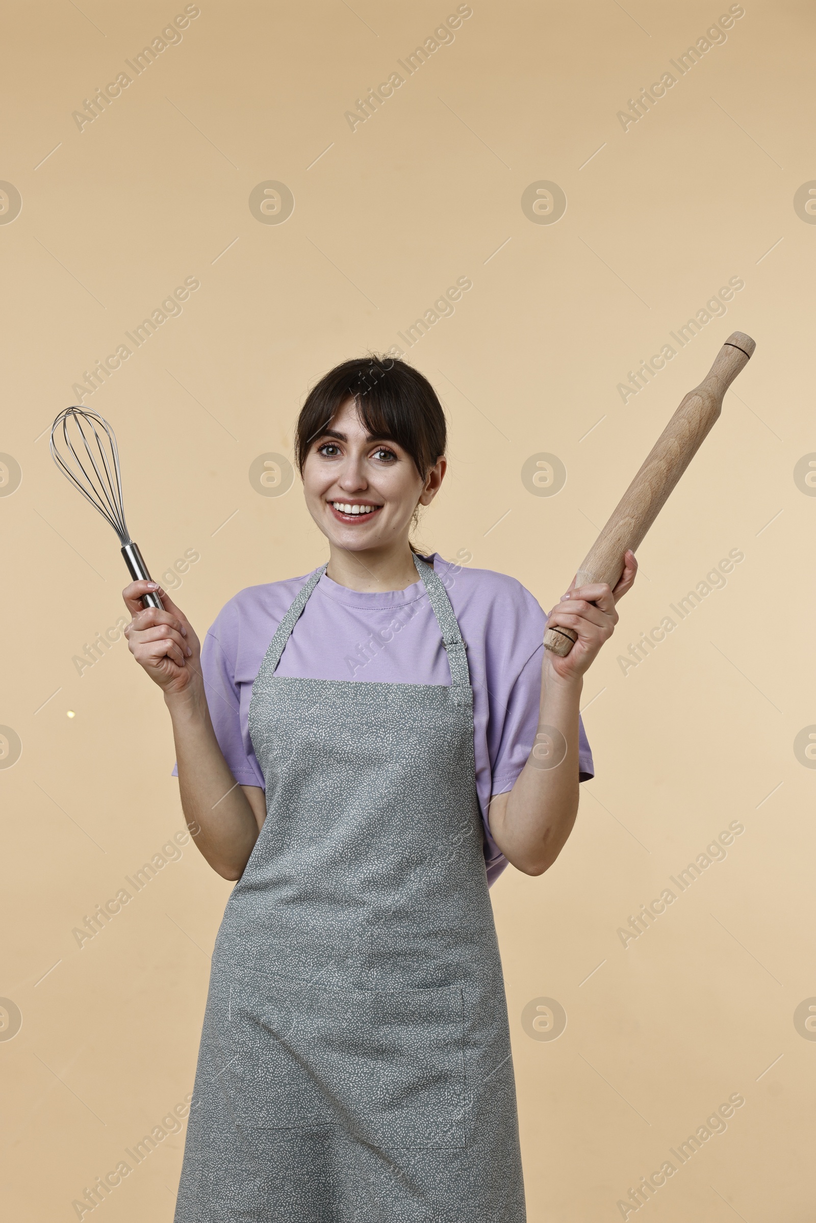 Photo of Woman with rolling pin and whisk on beige background