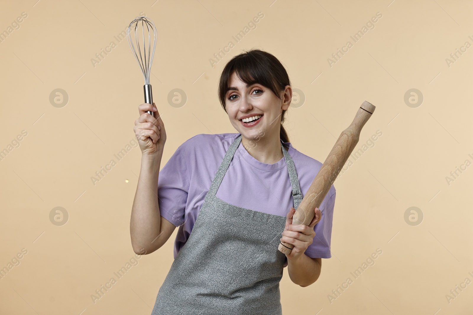 Photo of Woman with rolling pin and whisk on beige background