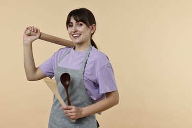 Photo of Happy woman with rolling pin, turner and spoon on beige background. Space for text