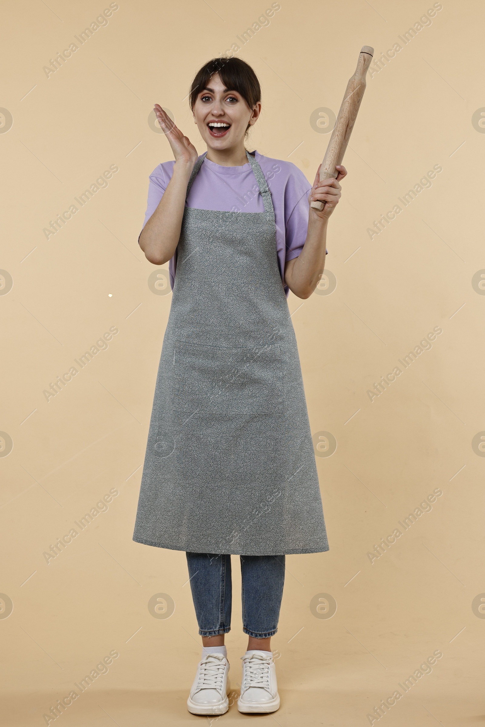 Photo of Excited woman with rolling pin on beige background