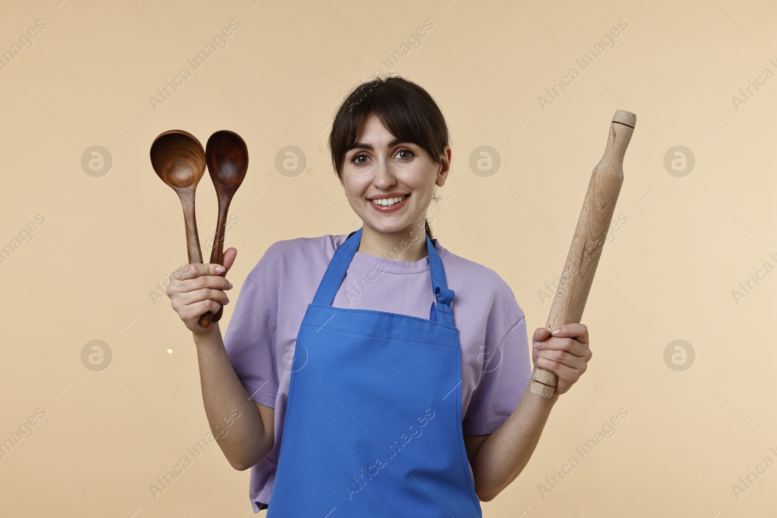 Photo of Happy woman with kitchen utensils on beige background