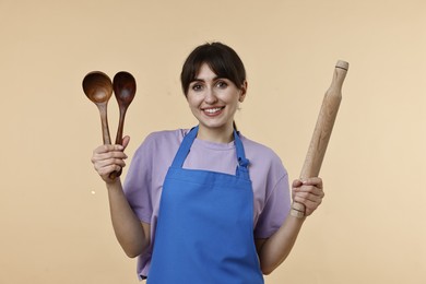 Photo of Happy woman with kitchen utensils on beige background