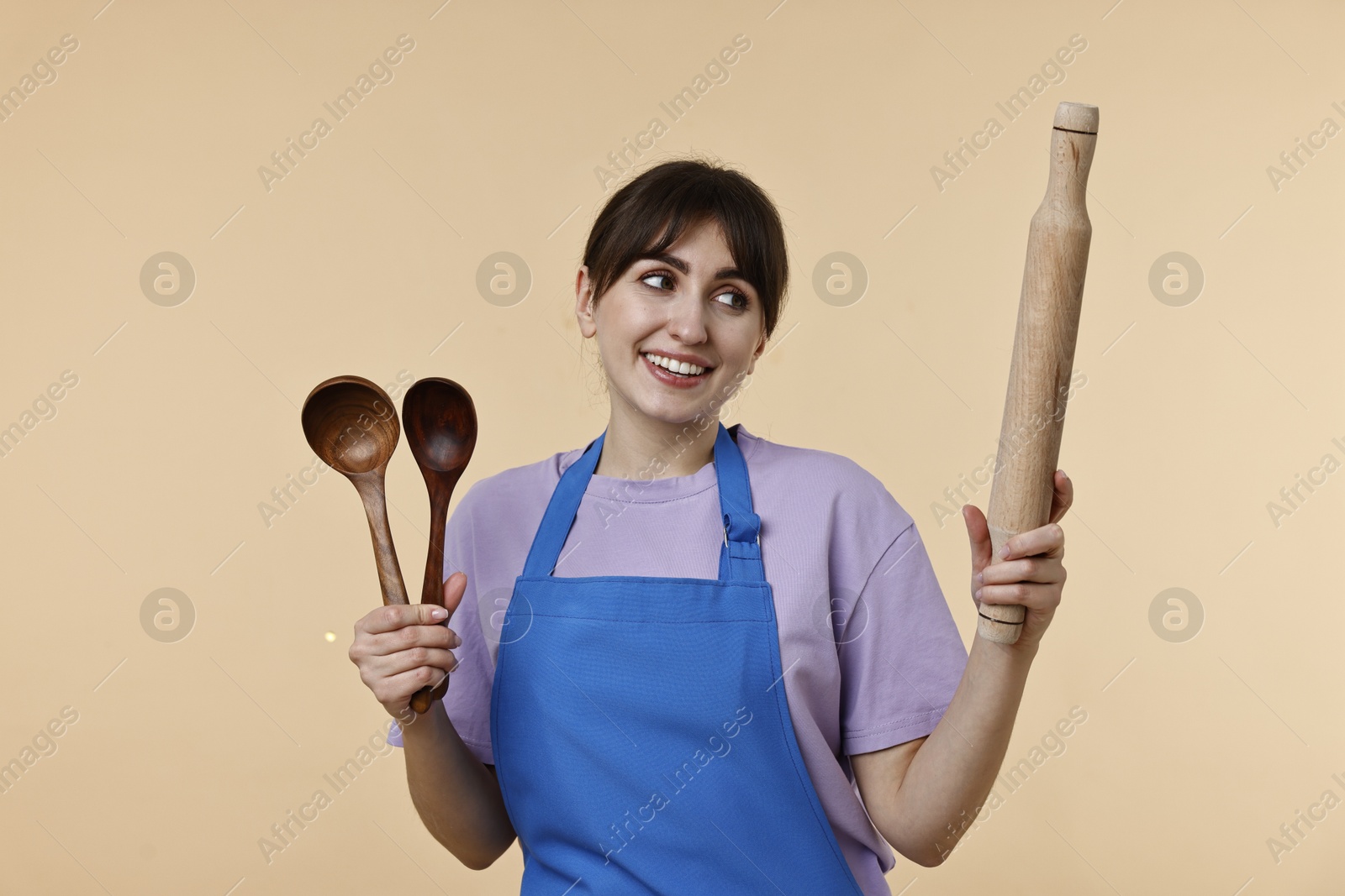 Photo of Happy woman with kitchen utensils on beige background