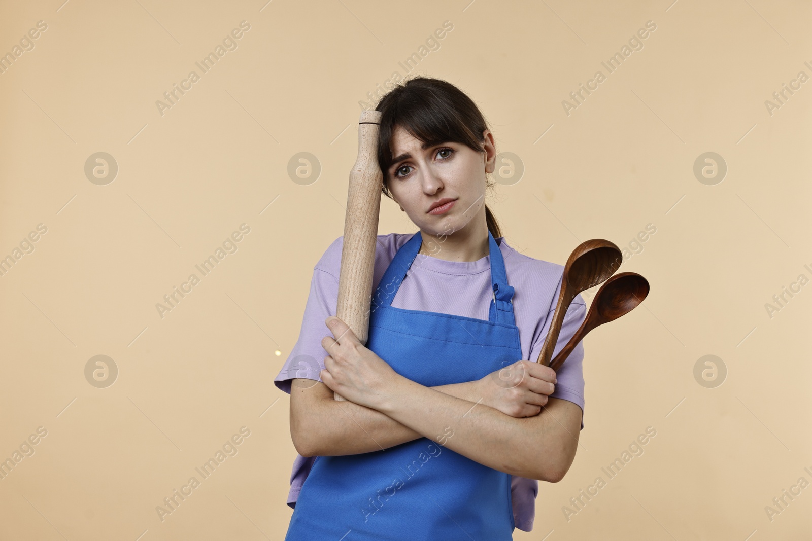 Photo of Upset woman with kitchen utensils on beige background