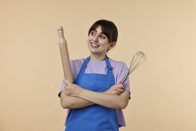 Photo of Happy woman with rolling pin and whisk on beige background