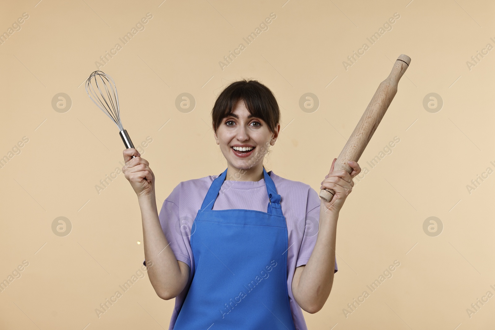 Photo of Happy woman with rolling pin and whisk on beige background