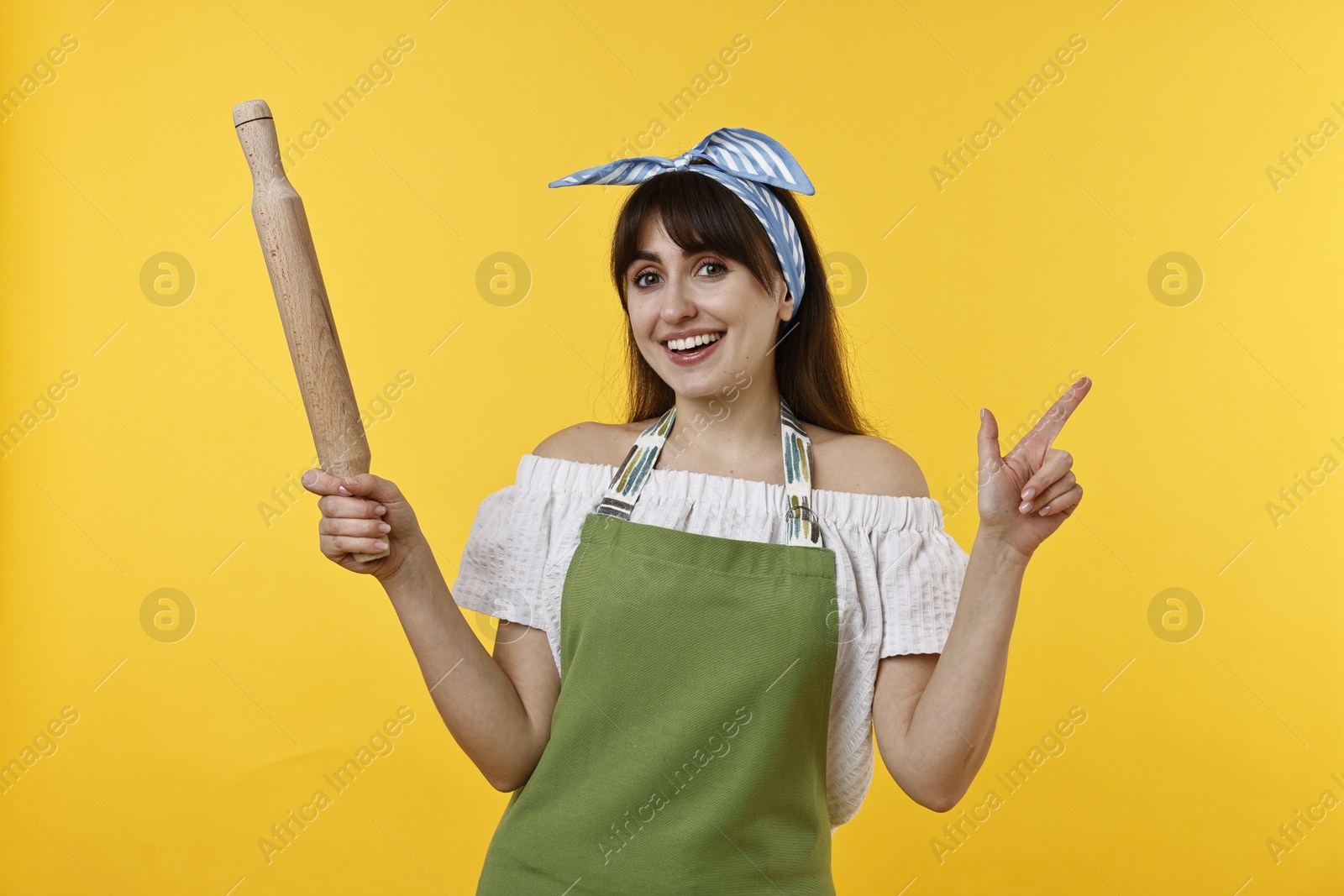 Photo of Woman with rolling pin pointing at something on yellow background