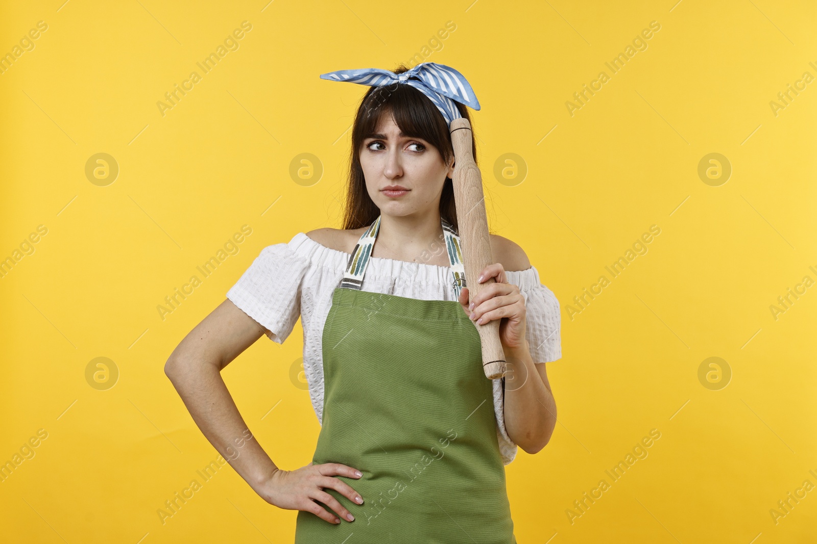 Photo of Upset woman with rolling pin on yellow background