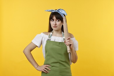 Upset woman with rolling pin on yellow background