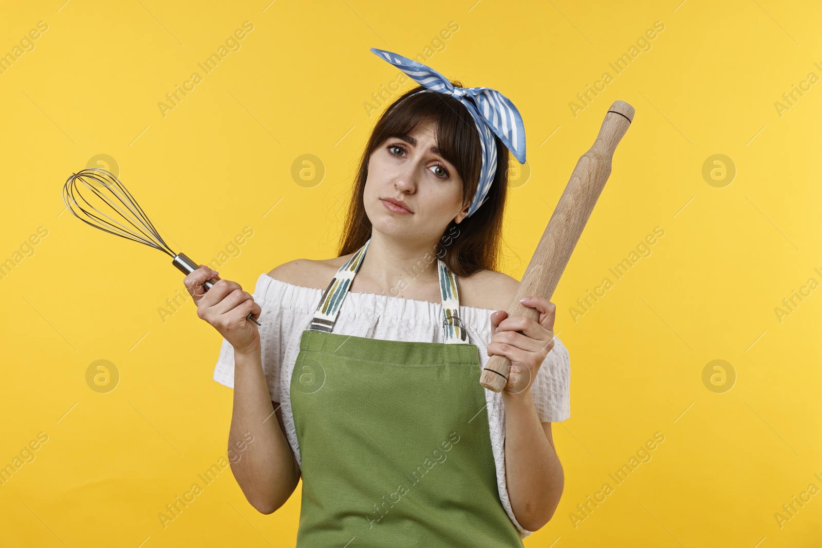 Photo of Upset woman with rolling pin and whisk on yellow background