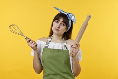 Photo of Upset woman with rolling pin and whisk on yellow background