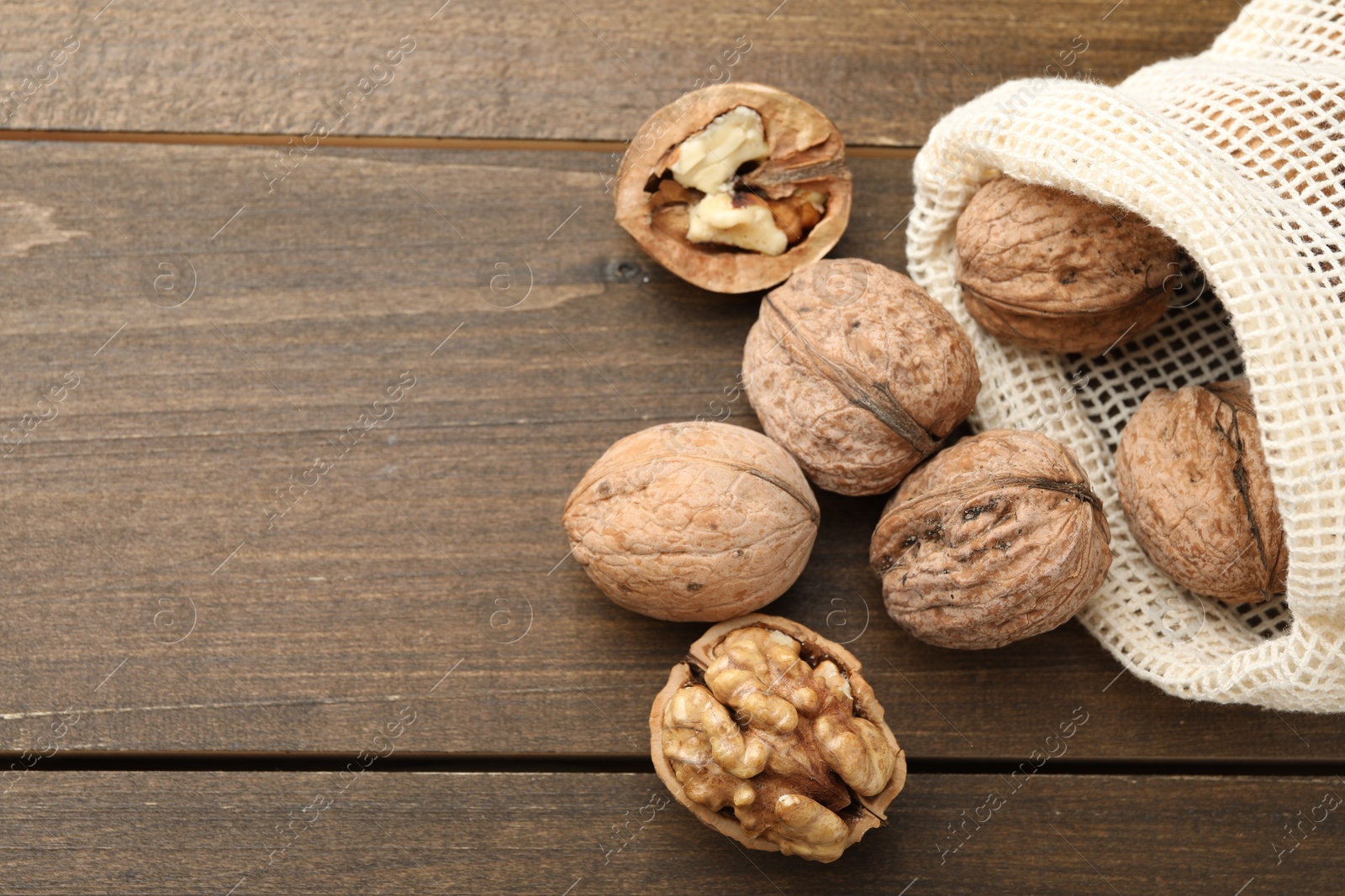 Photo of Fresh walnuts and bag on wooden table, flat lay. Space for text