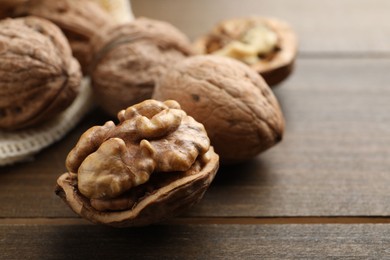 Photo of Fresh walnuts with shells on wooden table, closeup. Space for text