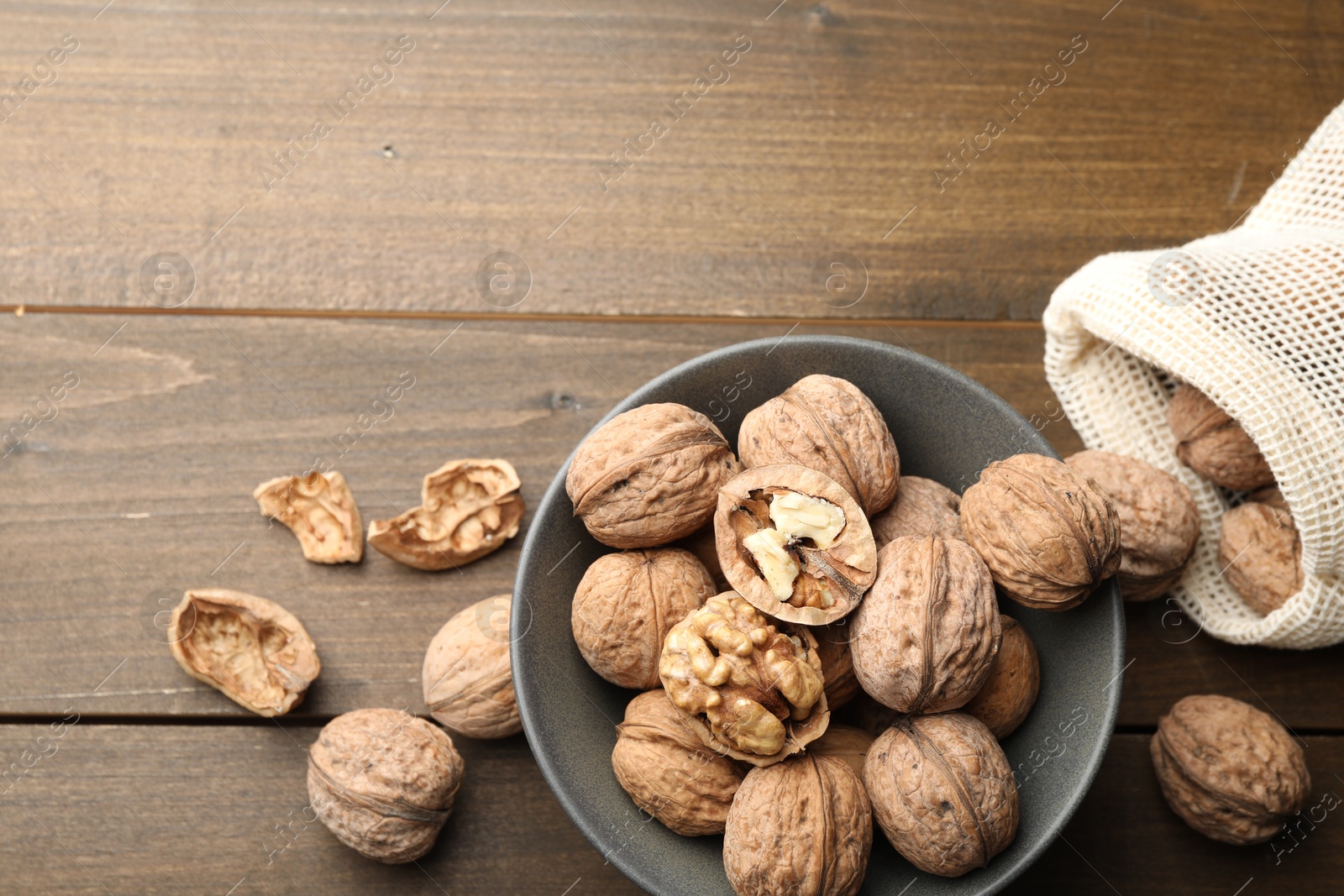 Photo of Fresh walnuts in bowl and bag on wooden table, flat lay. Space for text