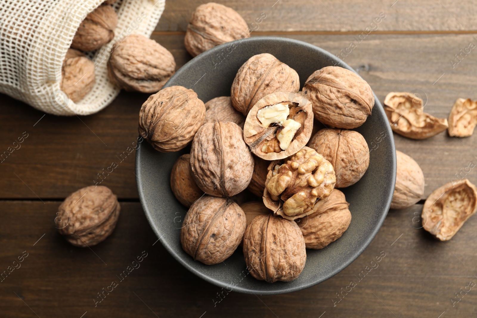 Photo of Fresh walnuts in bowl and bag on wooden table, flat lay