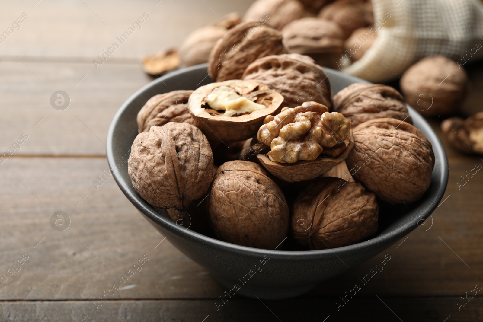 Photo of Fresh walnuts in bowl on wooden table, closeup