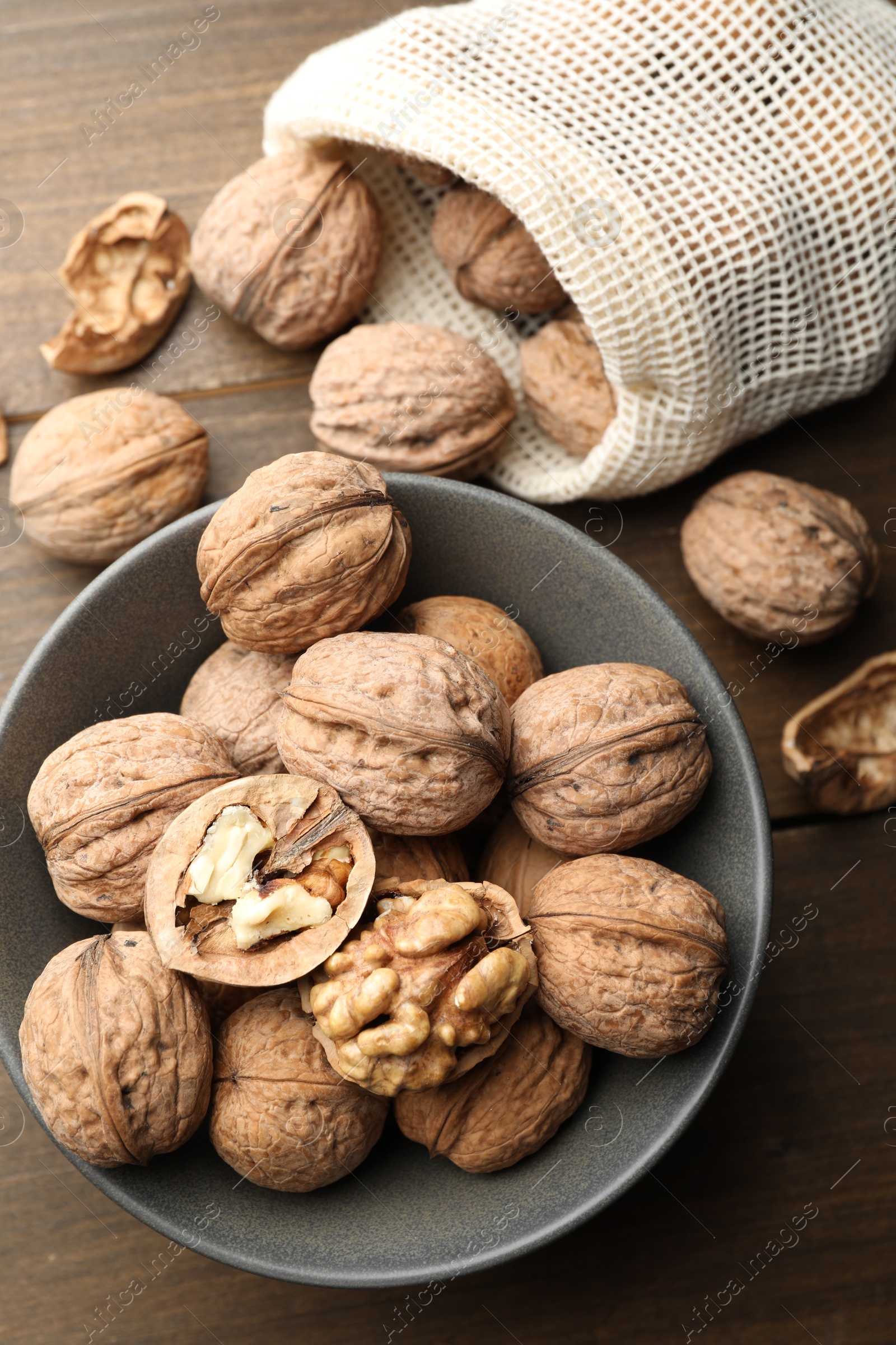 Photo of Fresh walnuts in bowl and bag on wooden table, flat lay