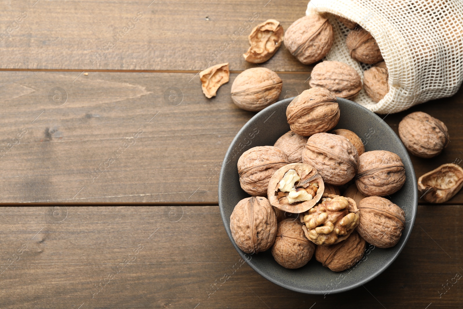 Photo of Fresh walnuts in bowl and bag on wooden table, flat lay. Space for text