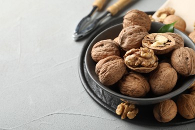 Photo of Fresh walnuts in bowl and nutcracker on gray textured table, closeup. Space for text