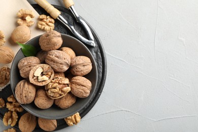 Photo of Fresh walnuts in bowl and nutcracker on gray textured table, flat lay. Space for text