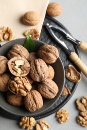 Photo of Fresh walnuts in bowl and nutcracker on gray table, flat lay