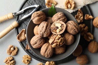 Photo of Fresh walnuts in bowl and nutcracker on gray table, flat lay