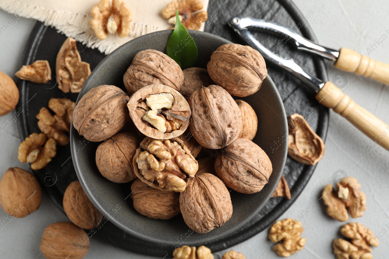 Photo of Fresh walnuts in bowl and nutcracker on gray table, flat lay