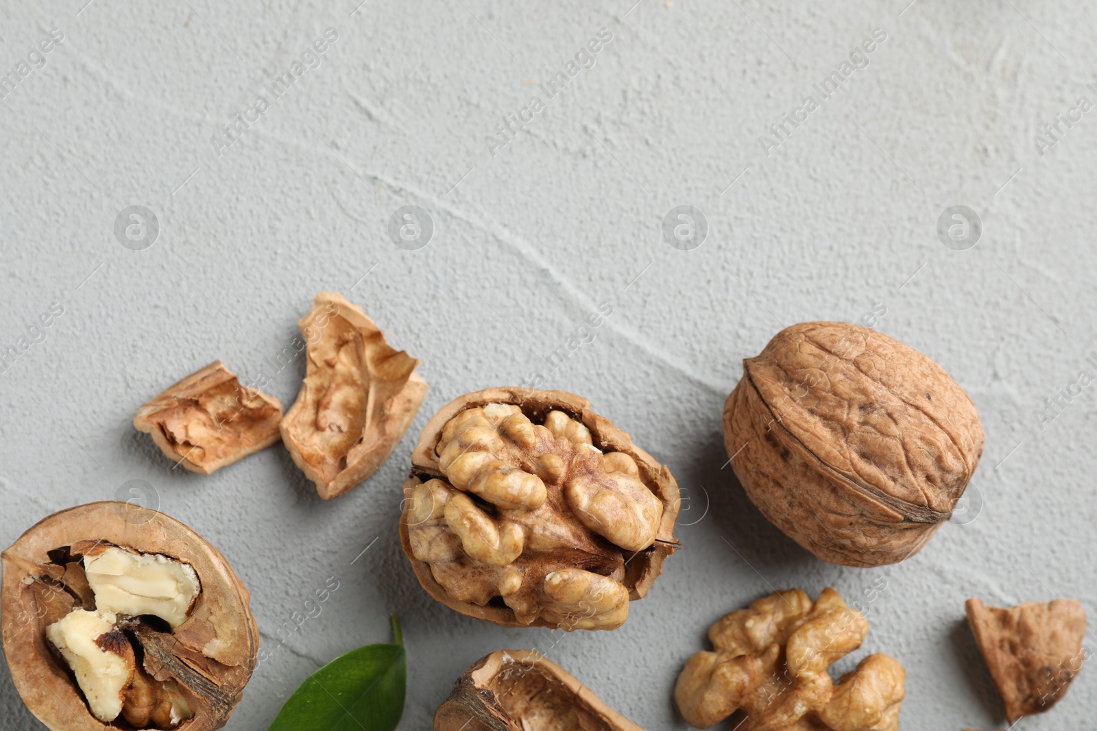 Photo of Fresh walnuts with shells on gray textured table, flat lay. Space for text