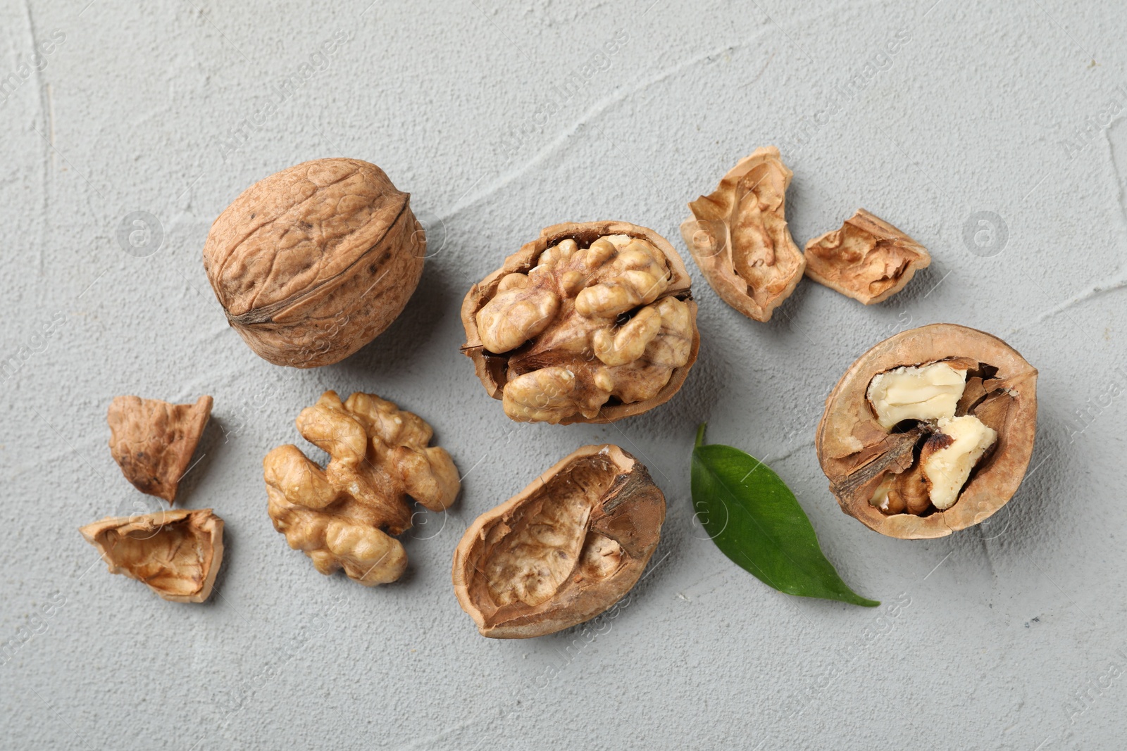 Photo of Fresh walnuts with shells and green leaf on gray textured table, flat lay