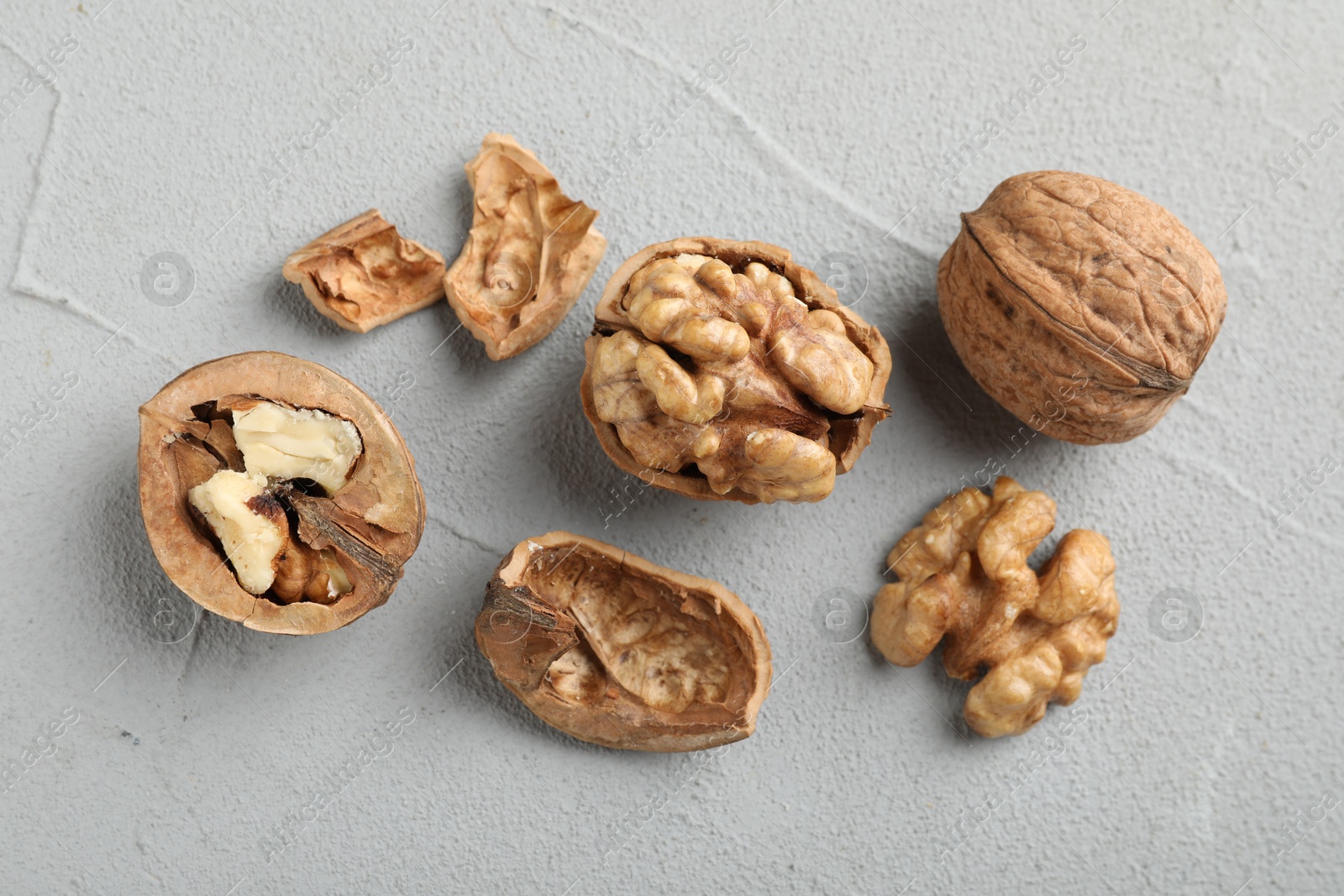 Photo of Fresh walnuts with shells on gray textured table, flat lay