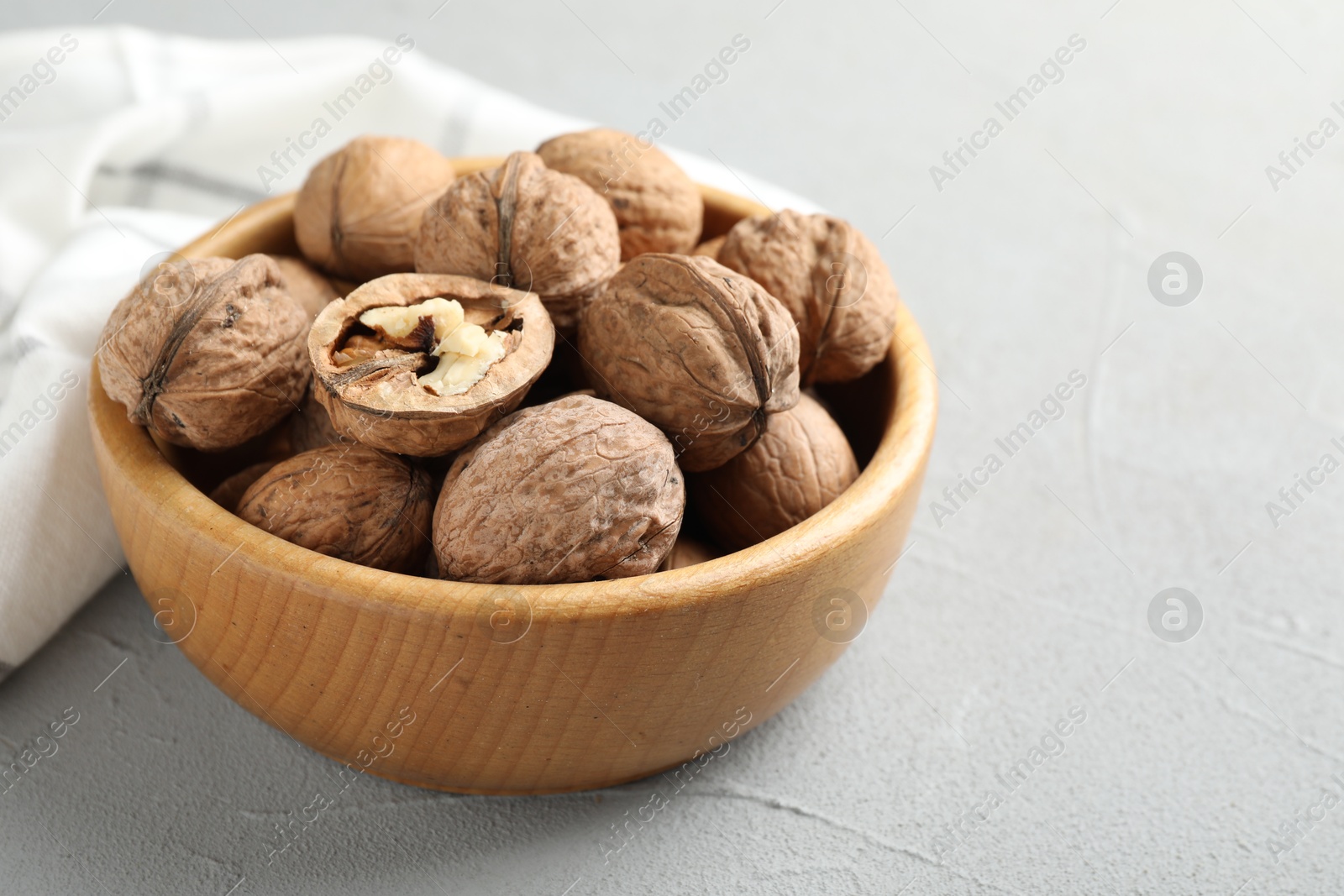 Photo of Fresh walnuts in bowl on gray table, closeup. Space for text