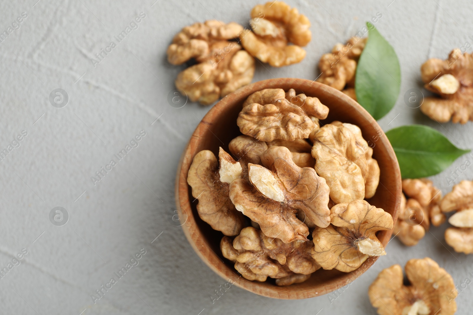 Photo of Peeled walnuts in bowl on gray textured table, flat lay. Space for text