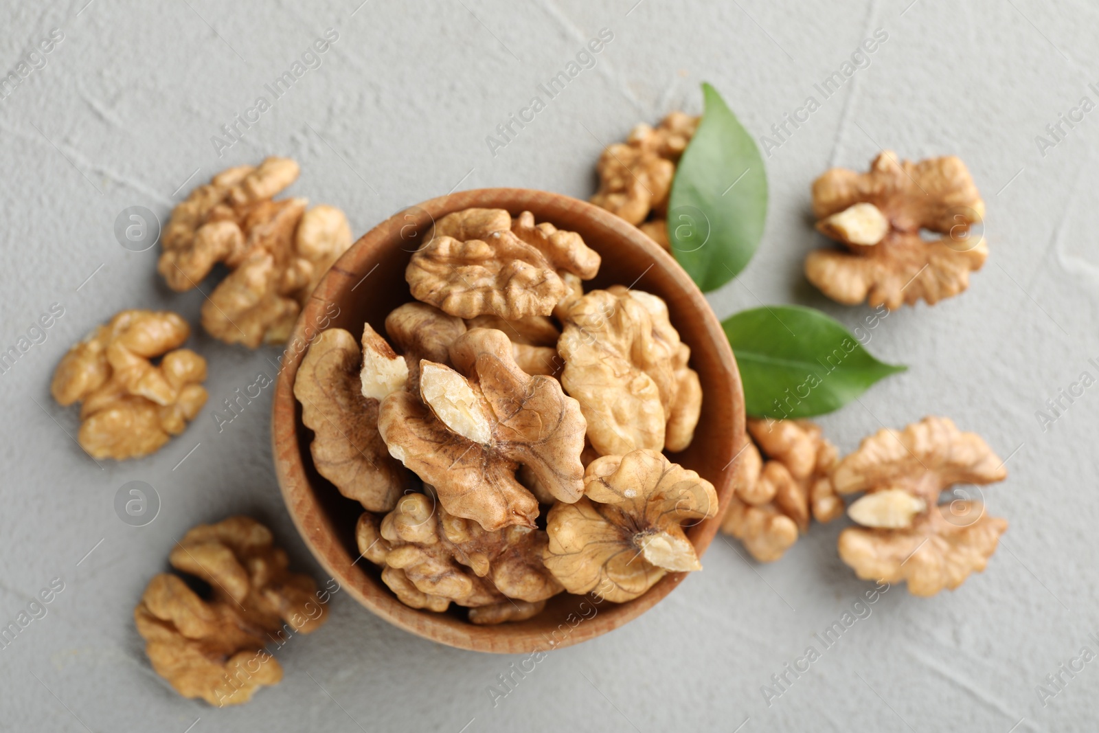 Photo of Peeled walnuts in bowl and green leaves on table, flat lay