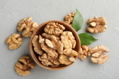 Photo of Peeled walnuts in bowl and green leaves on table, flat lay