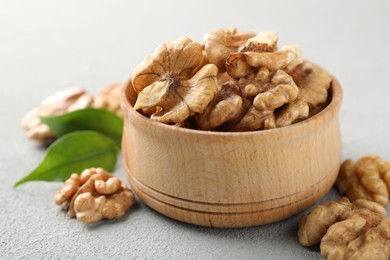 Photo of Peeled walnuts in bowl on gray textured table, closeup