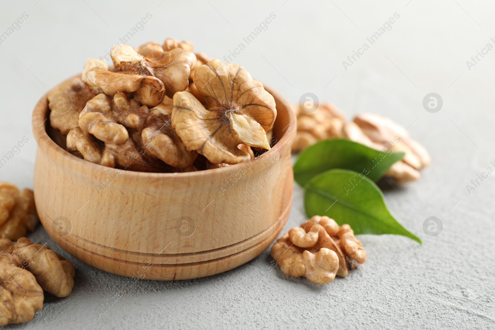 Photo of Peeled walnuts in bowl on gray textured table, closeup. Space for text