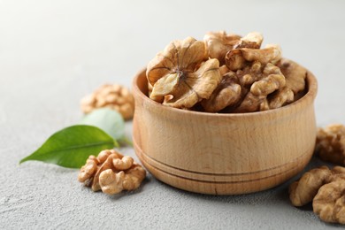 Photo of Peeled walnuts in bowl on gray textured table, closeup. Space for text