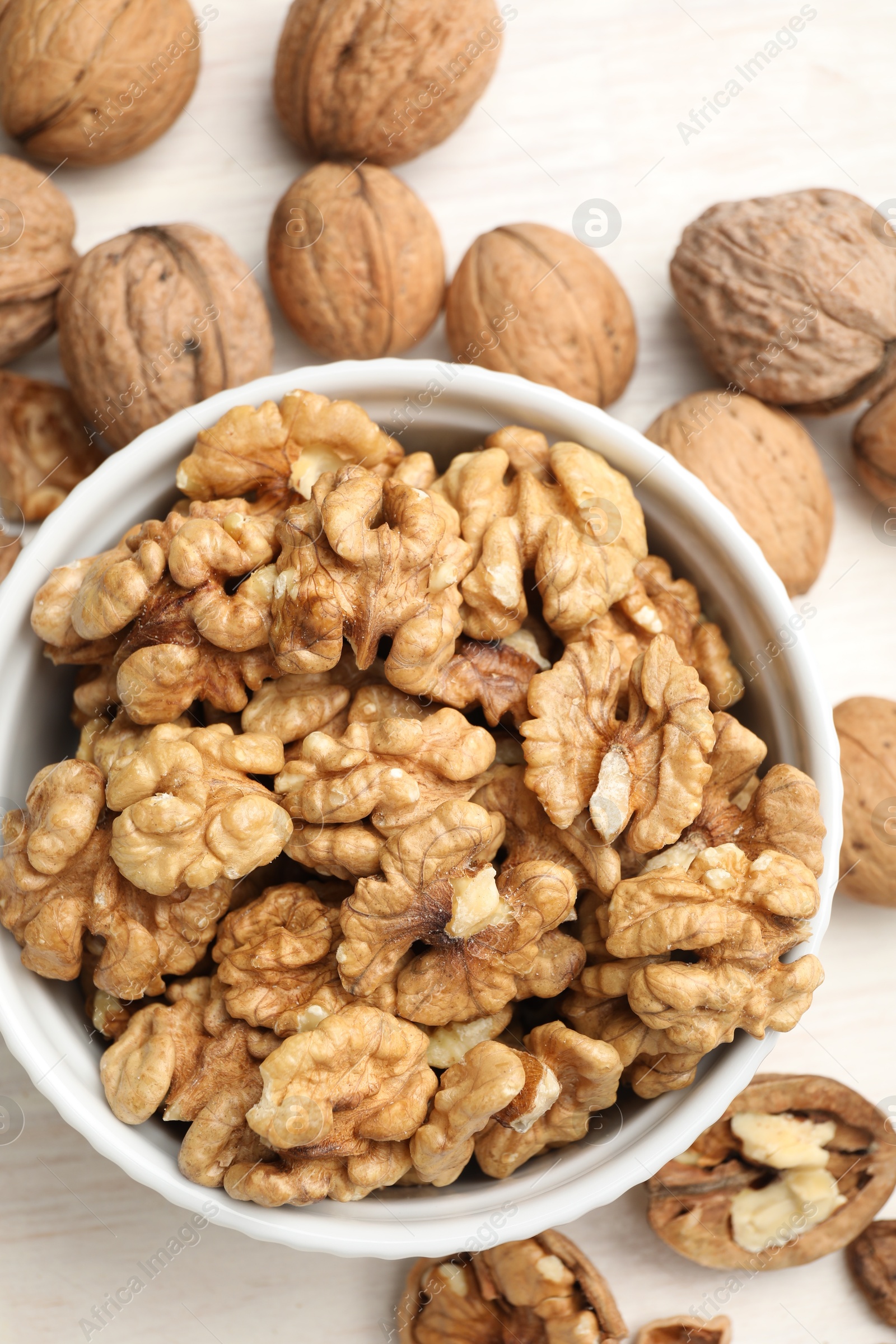 Photo of Peeled walnuts in bowl on light table, flat lay