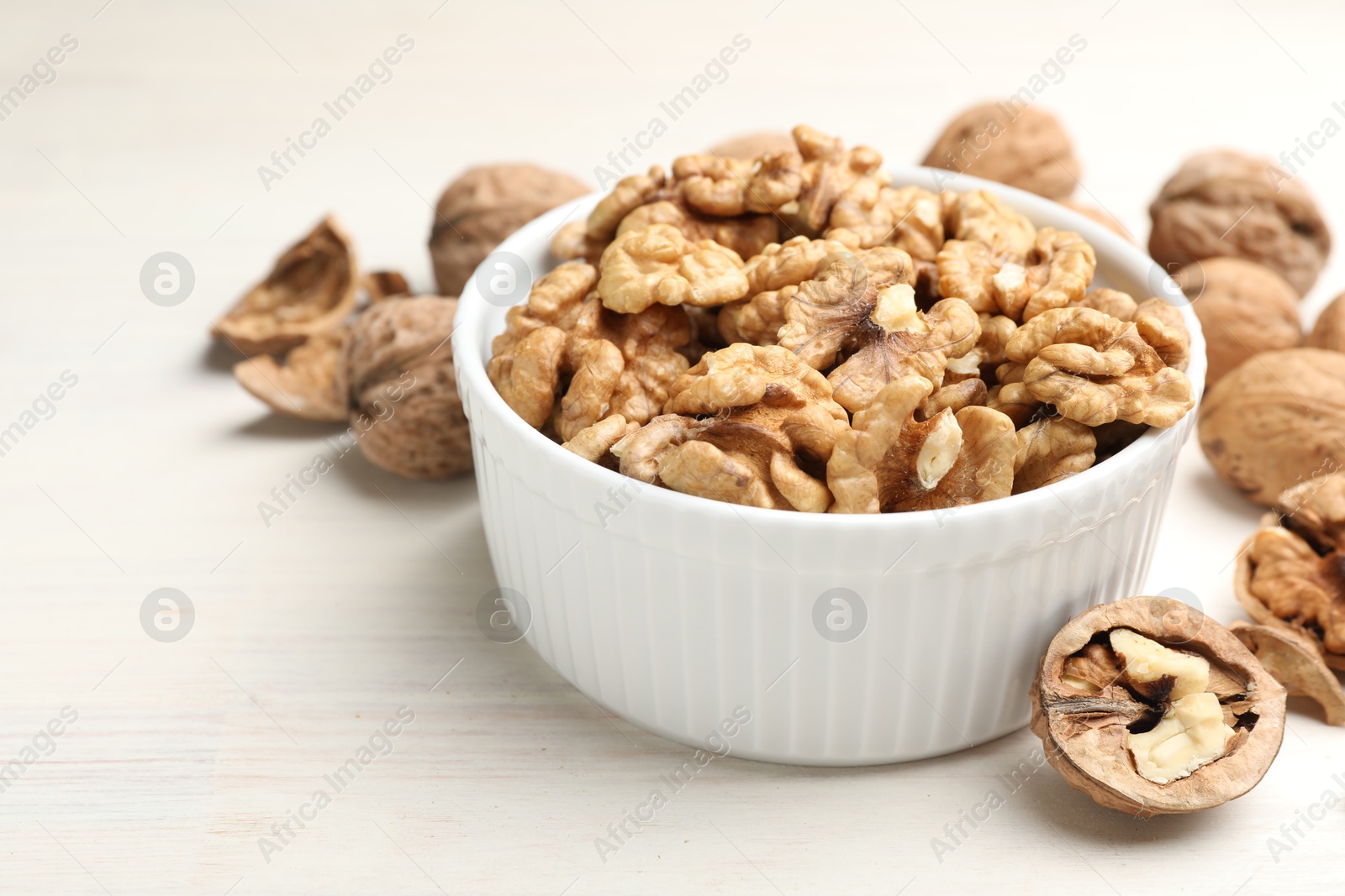 Photo of Peeled walnuts in bowl on light wooden table, closeup. Space for text