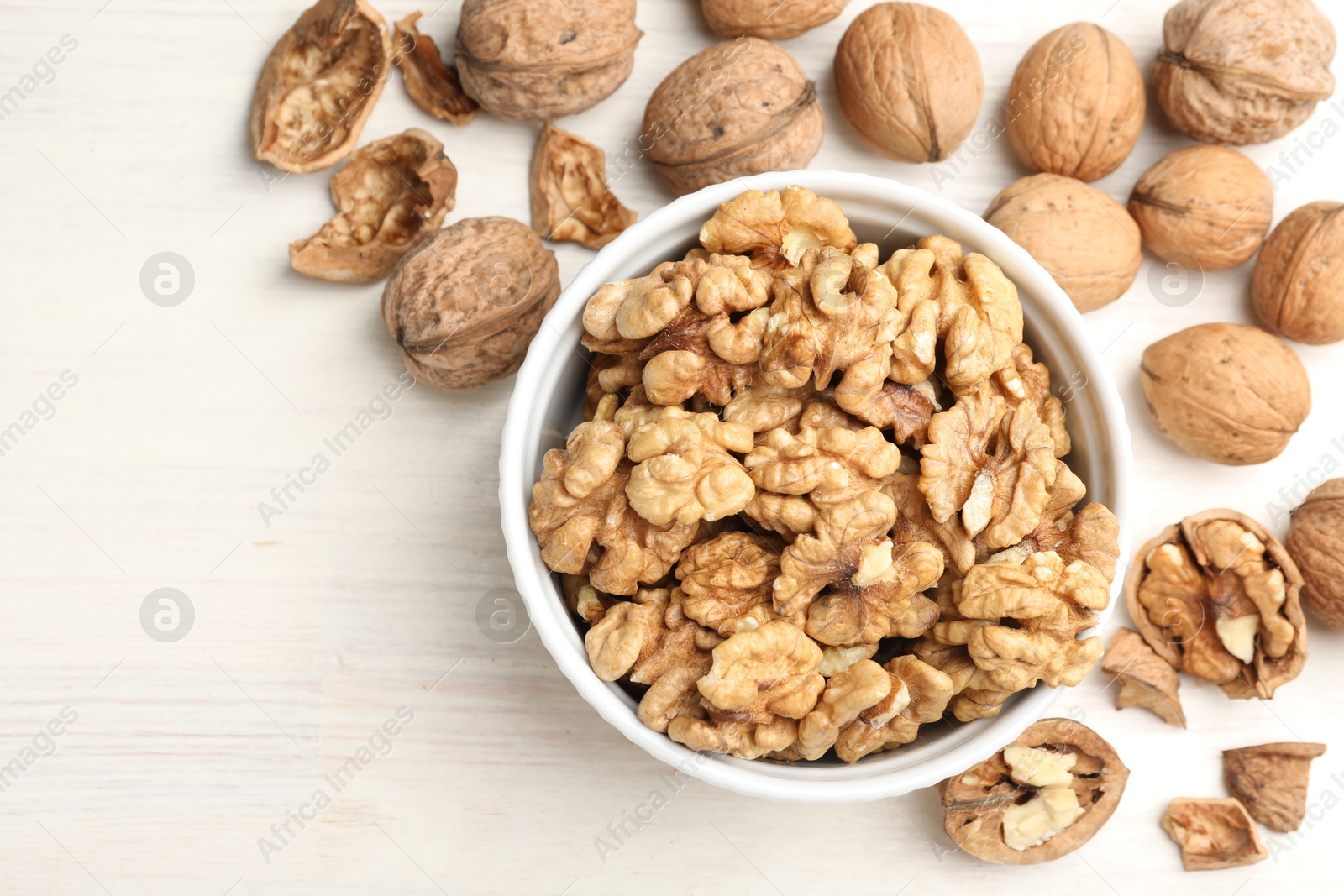 Photo of Peeled walnuts in bowl and whole ones on light wooden table, flat lay. Space for text