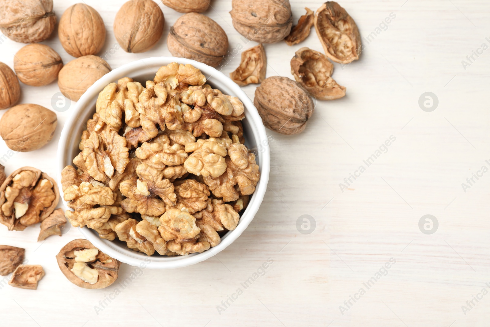 Photo of Peeled walnuts in bowl and whole ones on light wooden table, flat lay. Space for text