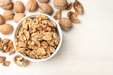 Photo of Peeled walnuts in bowl and whole ones on light wooden table, flat lay. Space for text