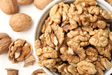 Photo of Peeled walnuts in bowl and whole ones on light table, flat lay