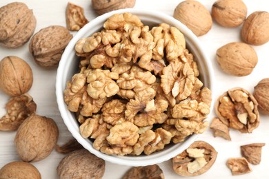 Photo of Peeled walnuts in bowl and whole ones on light table, flat lay